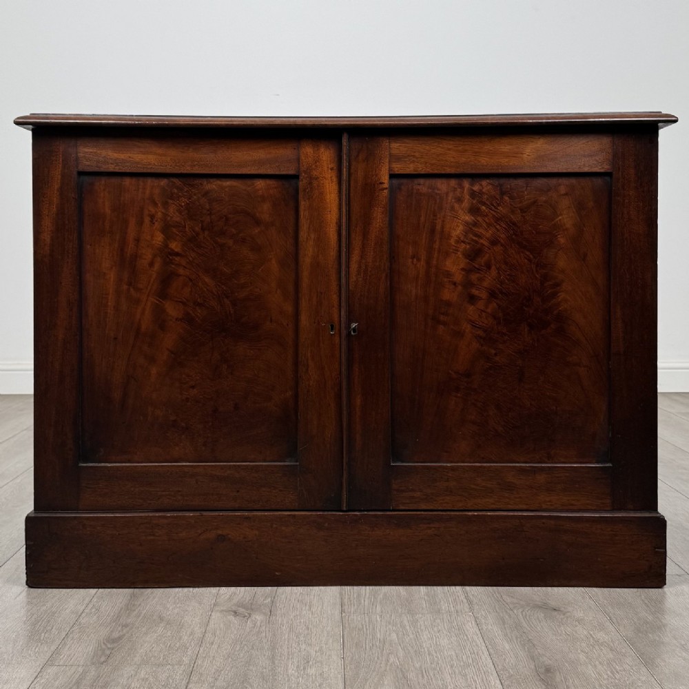 A Victorian mahogany collectors cabinet featuring flame mahogany twin panel doors and a wide plinth base.
