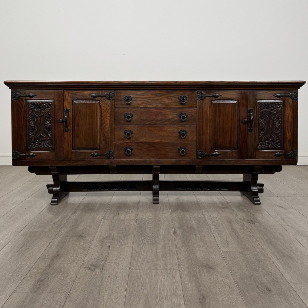 A large dark carved oak sideboard featuring panelled cupboard doors with iron strap hinges, central drawers, and a carved low stretcher base.
