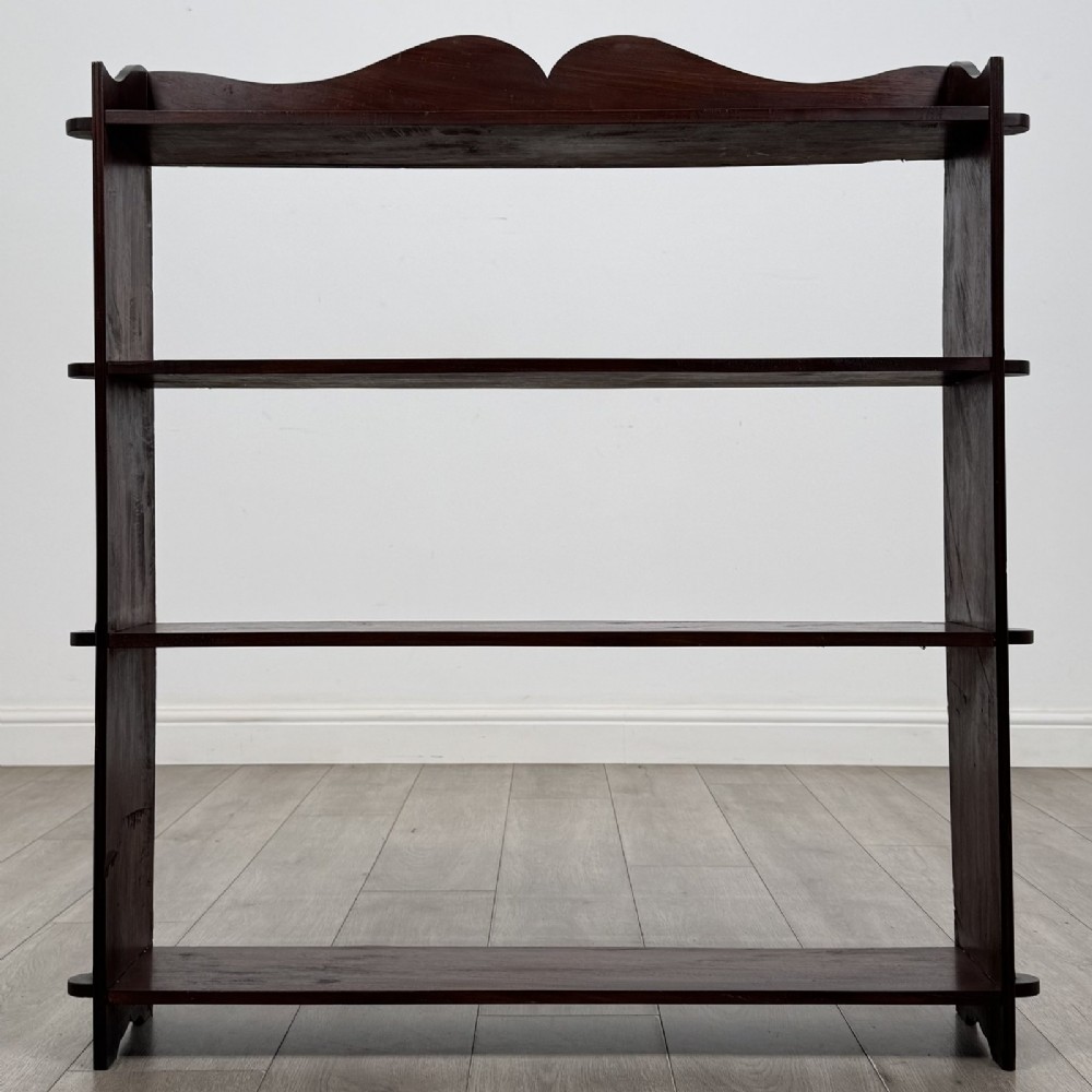 A dark mahogany open bookcase featuring four tiered open shelves and a shaped, scalloped raised gallery back.