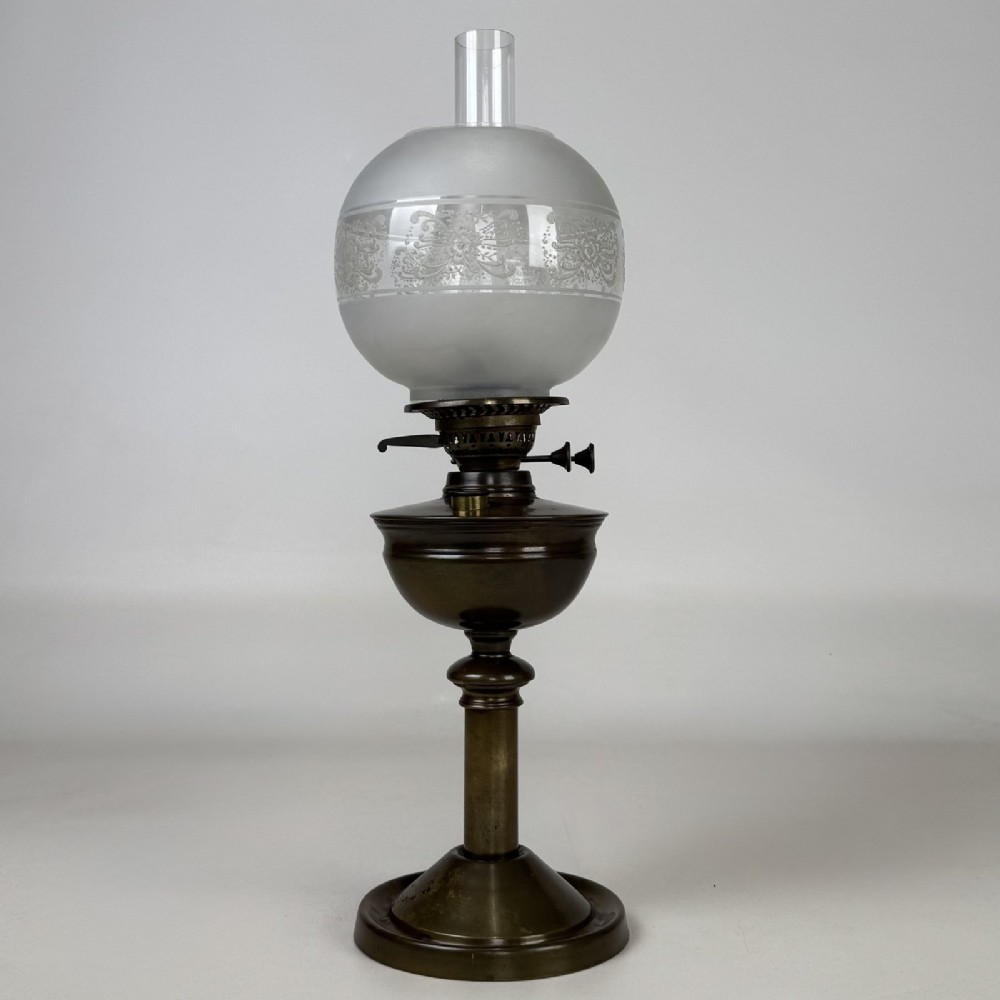 An antique Victorian brass oil lamp featuring a circular stepped base, a columnar pedestal supporting a round brass reservoir, a burner assembly, a spherical etched frosted glass shade, and a clear glass chimney.