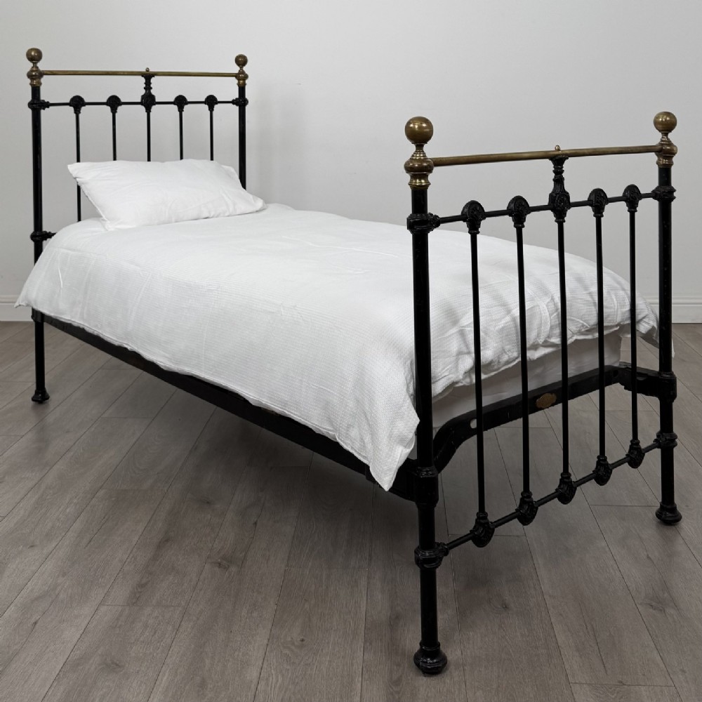 A Victorian single bed frame constructed from black cast iron spindles and topped with a brass top rail and ball finials.