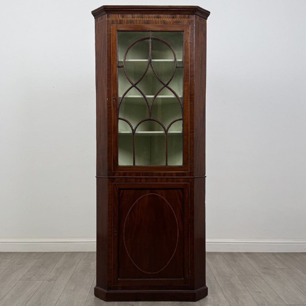 An 18th-century Georgian mahogany standing corner cabinet featuring an upper astragal glazed door and a lower solid panel door with oval inlay.