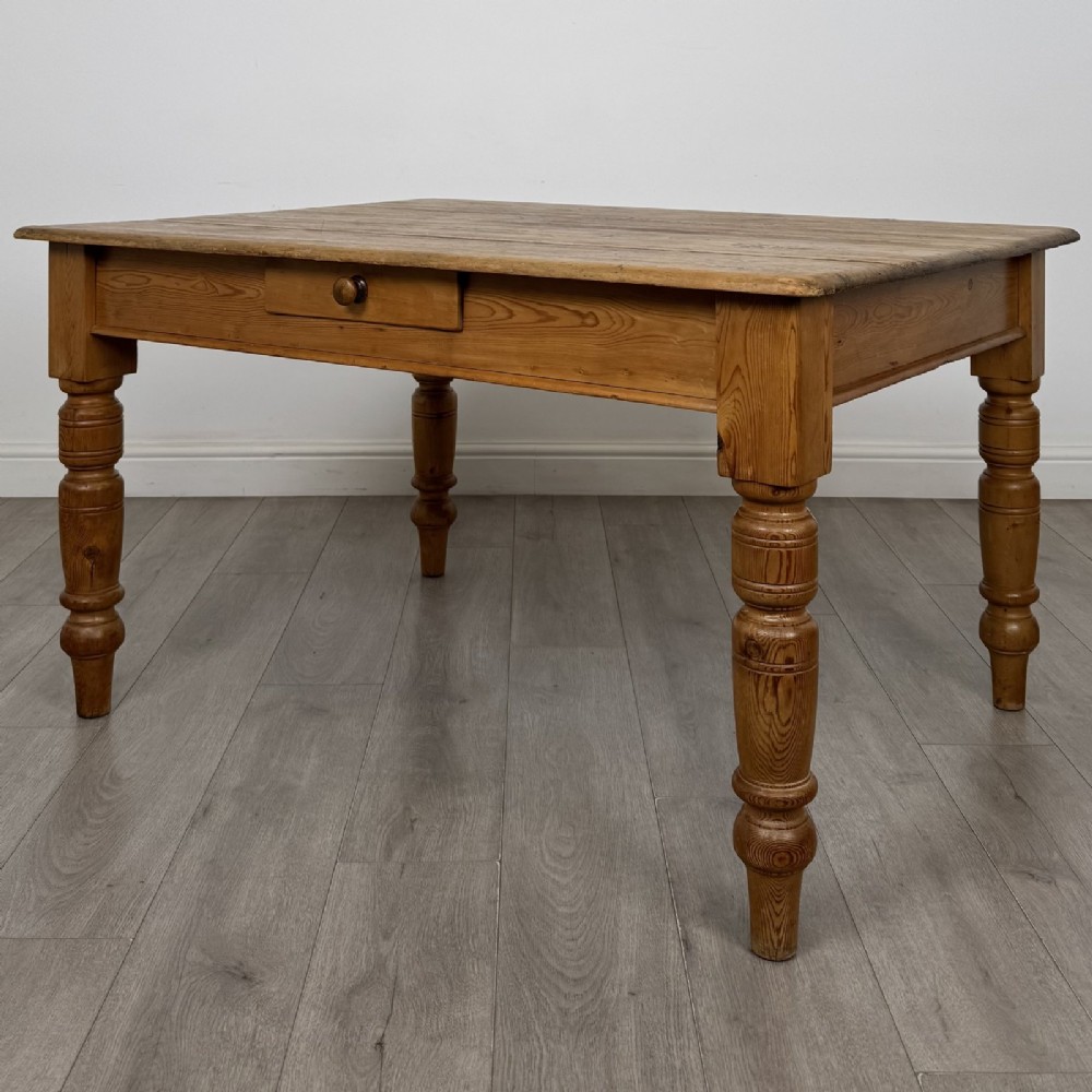 A rectangular pine dining table with four turned legs, a planked top, and a single frieze drawer with a wooden knob.
