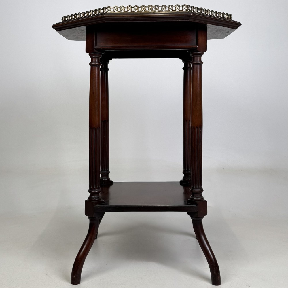 An octagonal dark mahogany side table featuring a pierced brass gallery top, turned fluted columns, a lower tier shelf, and splayed legs.