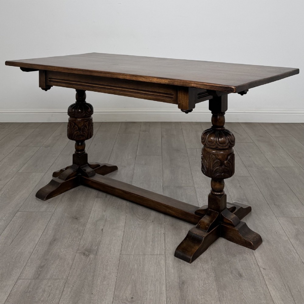 A dark oak refectory dining table featuring carved cup-and-cover legs joined by a floor-level stretcher.
