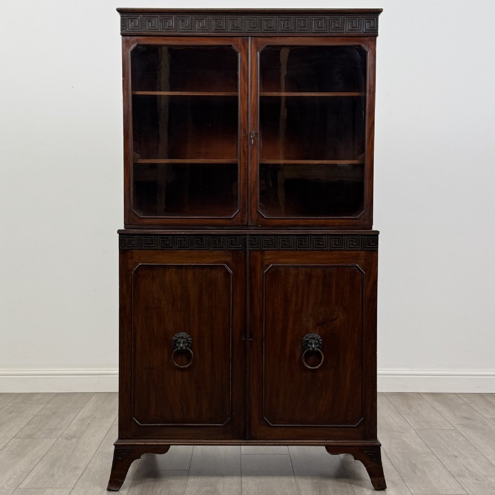 An eighteenth-century Georgian mahogany glazed bookcase featuring an upper cabinet with glass doors and a lower cabinet with carved doors, lion mask handles, and Greek key frieze details.