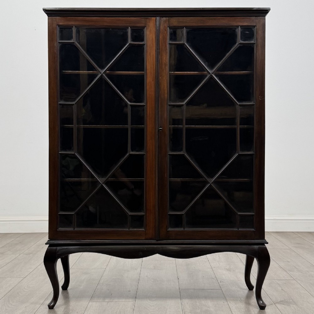 An Edwardian dark mahogany display cabinet featuring twin astragal glazed doors and shaped cabriole legs.