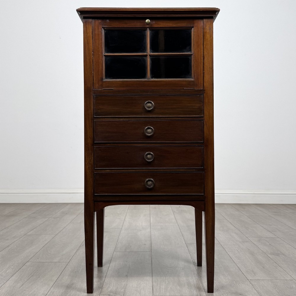 A tall, narrow Edwardian mahogany cabinet featuring a top four-pane glazed compartment above four stacked drawers, resting on slim tapered legs.