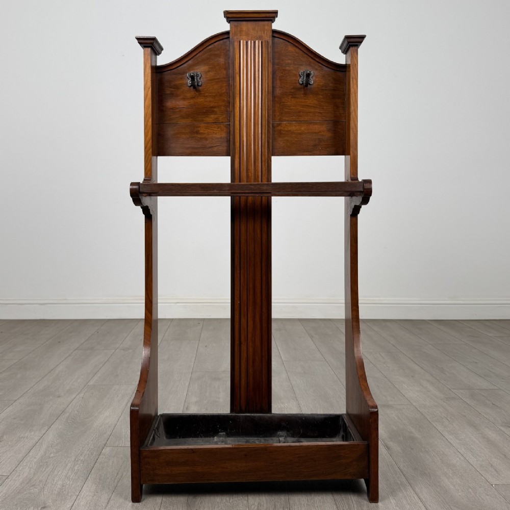 An Edwardian walnut hall stand featuring central fluted wood paneling, two metal hanging hooks, a stick retention bar, and a lower drip tray.