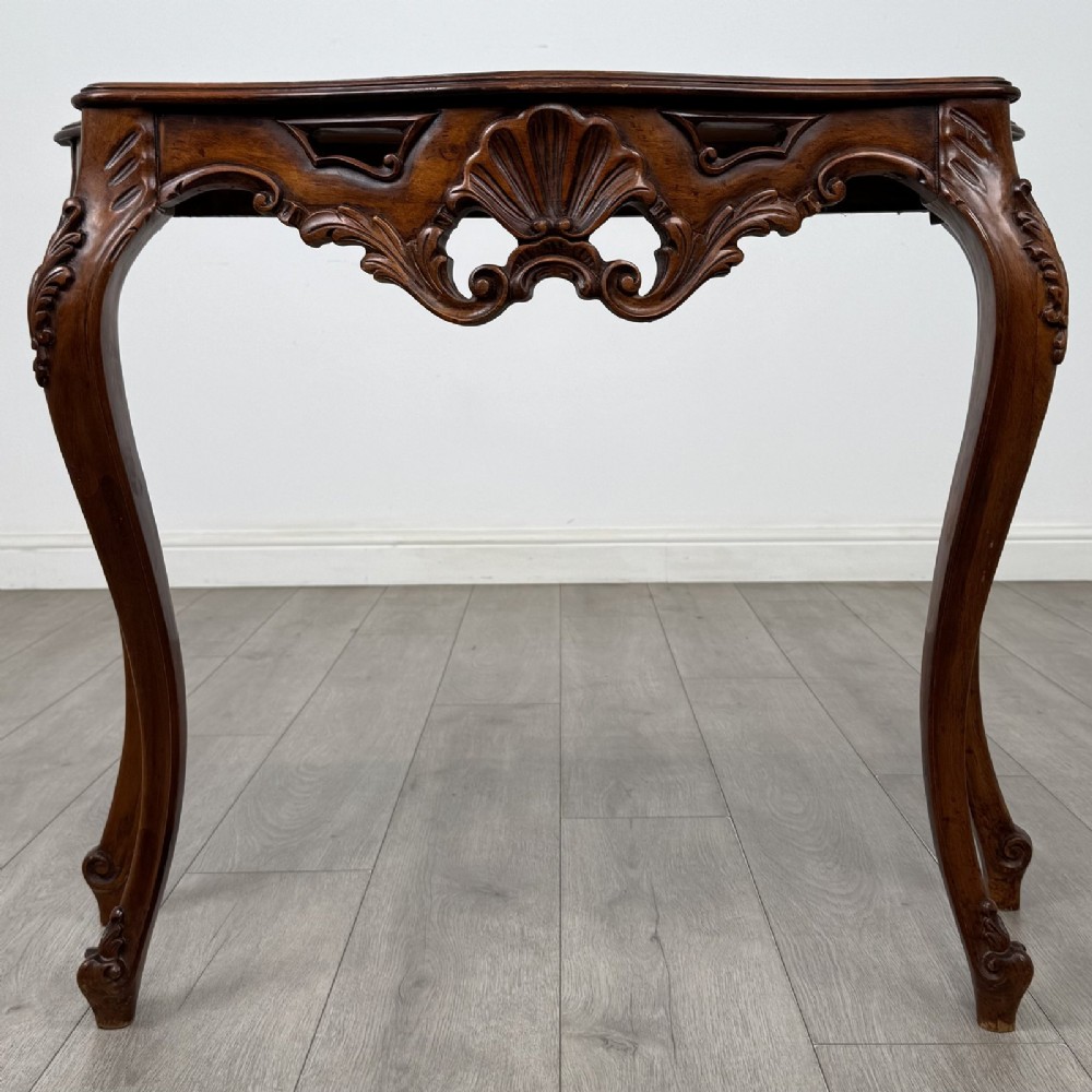 A carved mahogany French style side table featuring exaggerated cabriole legs, a shell motif apron, and a serpentine tabletop.