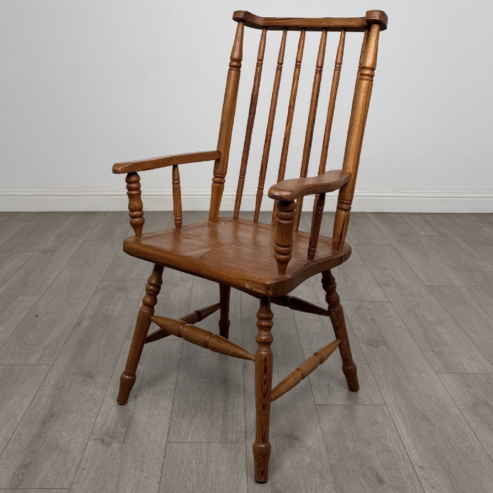 A pitch pine stick back armchair featuring vertical spindle uprights, turned legs, shaped armrests, and turned stretchers.