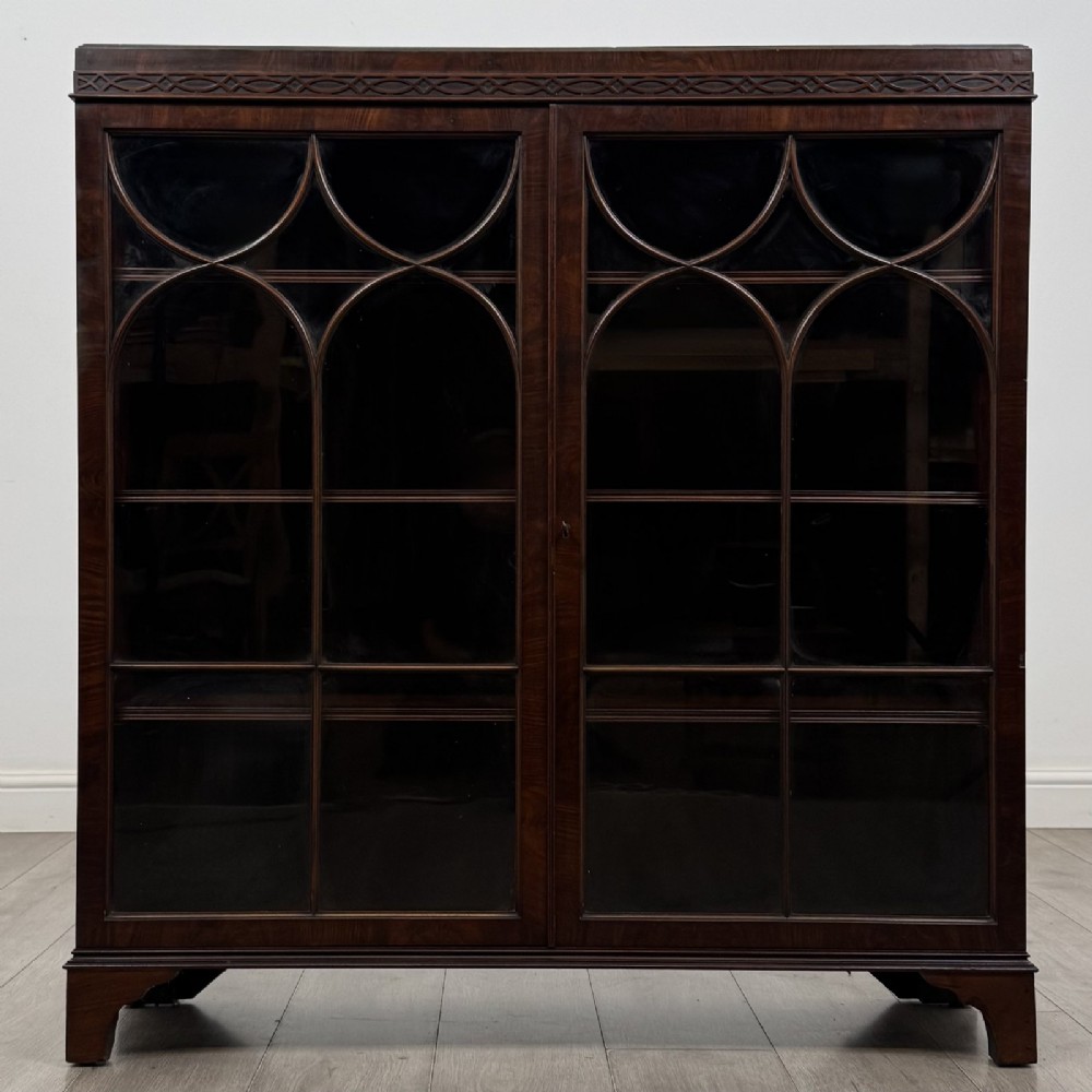 An Edwardian dark mahogany display cabinet featuring twin astragal glazed doors with Gothic tracery and bracket feet.
