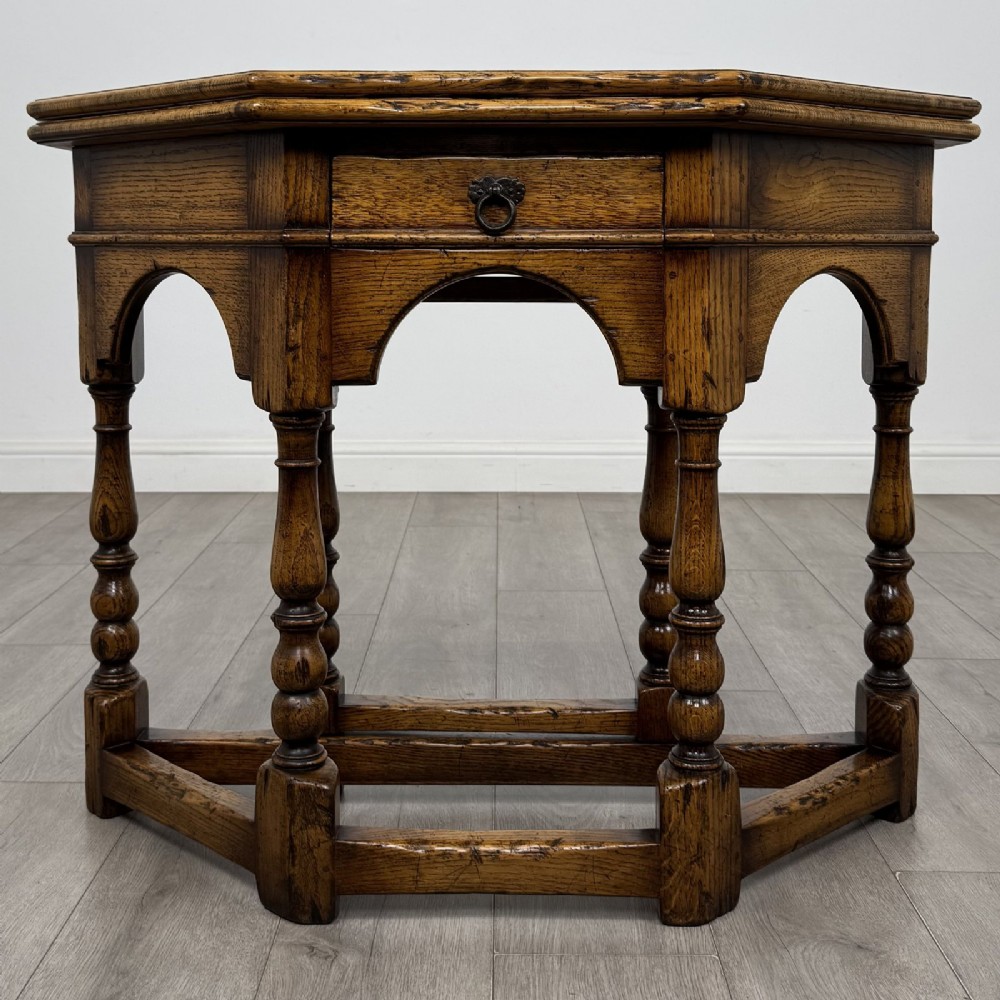 An early 20th-century golden oak fold-over tea table featuring an octagonal top, arched frieze with a single central drawer, turned legs, and lower stretchers.