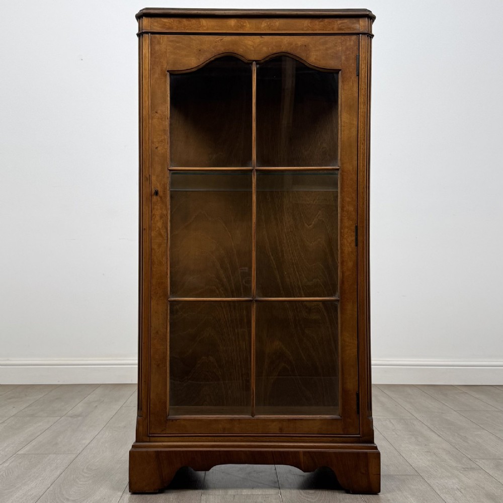 A standing burr walnut display cabinet with a single six-pane glass door and a bracket foot base.