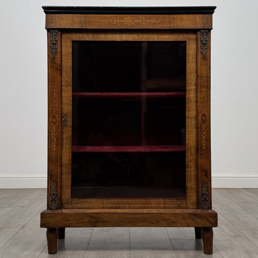A 19th-century Victorian walnut pier cabinet featuring floral marquetry inlays, decorative gilt metal mounts, a single glazed glass door, and velvet-lined interior shelves.