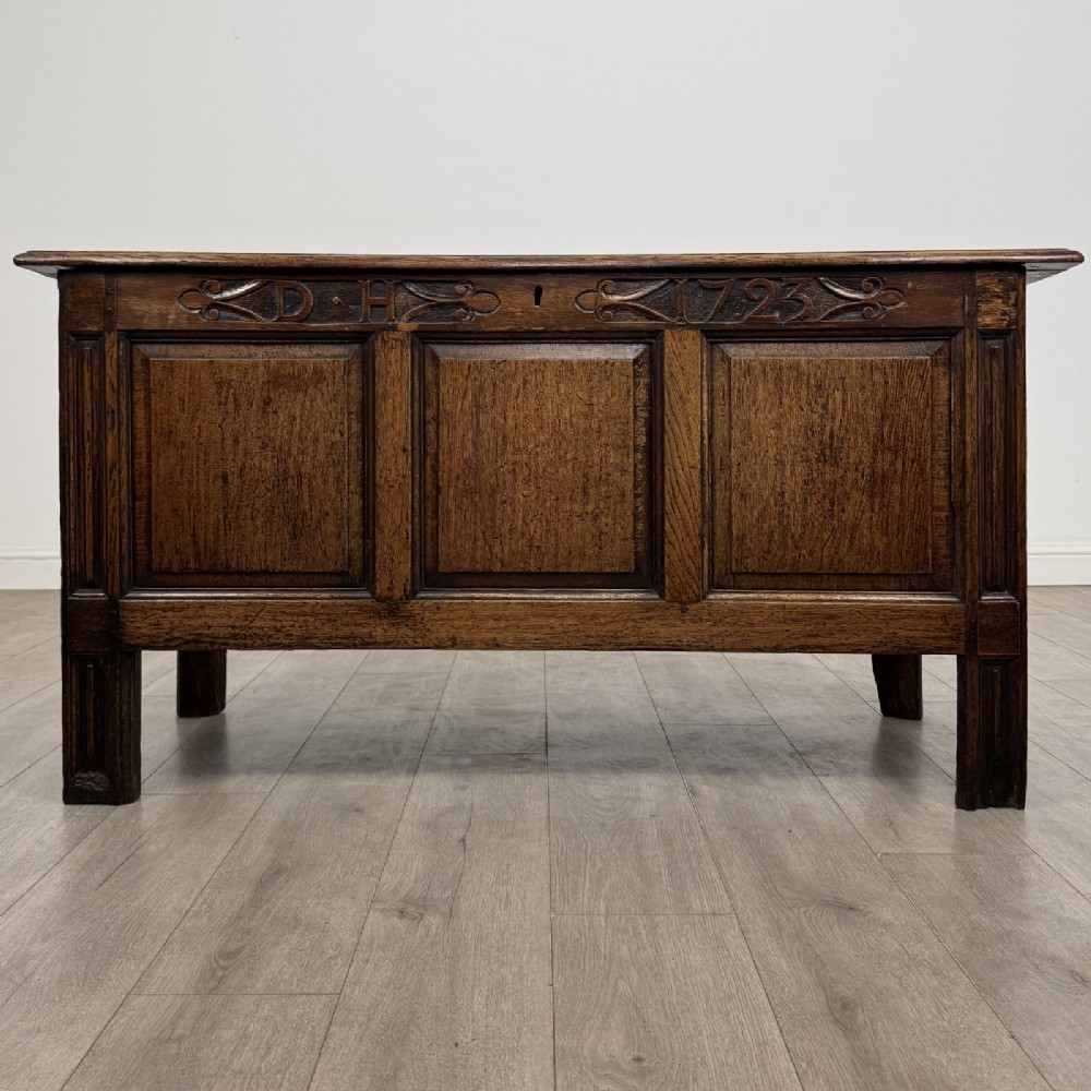 An antique early 18th-century panelled oak coffer featuring a carved frieze with initials D H and the year 1723.