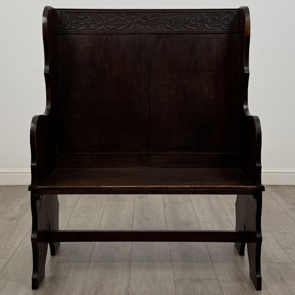 A dark carved oak high-back settle featuring a floral carved frieze across the top and shaped side armrests.