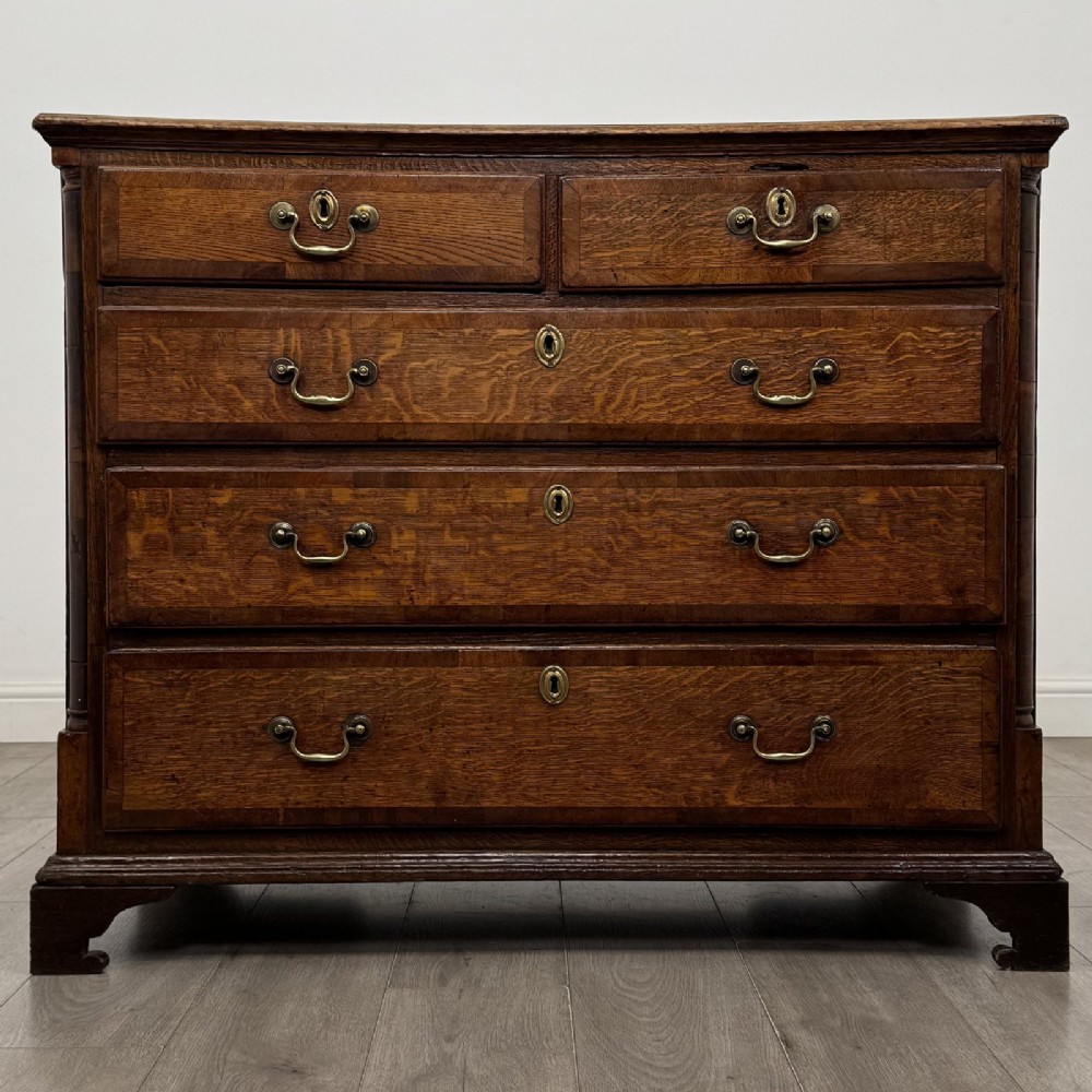 An eighteenth-century Georgian oak chest of drawers featuring two short drawers over three long drawers with brass swan-neck handles and bracket feet.