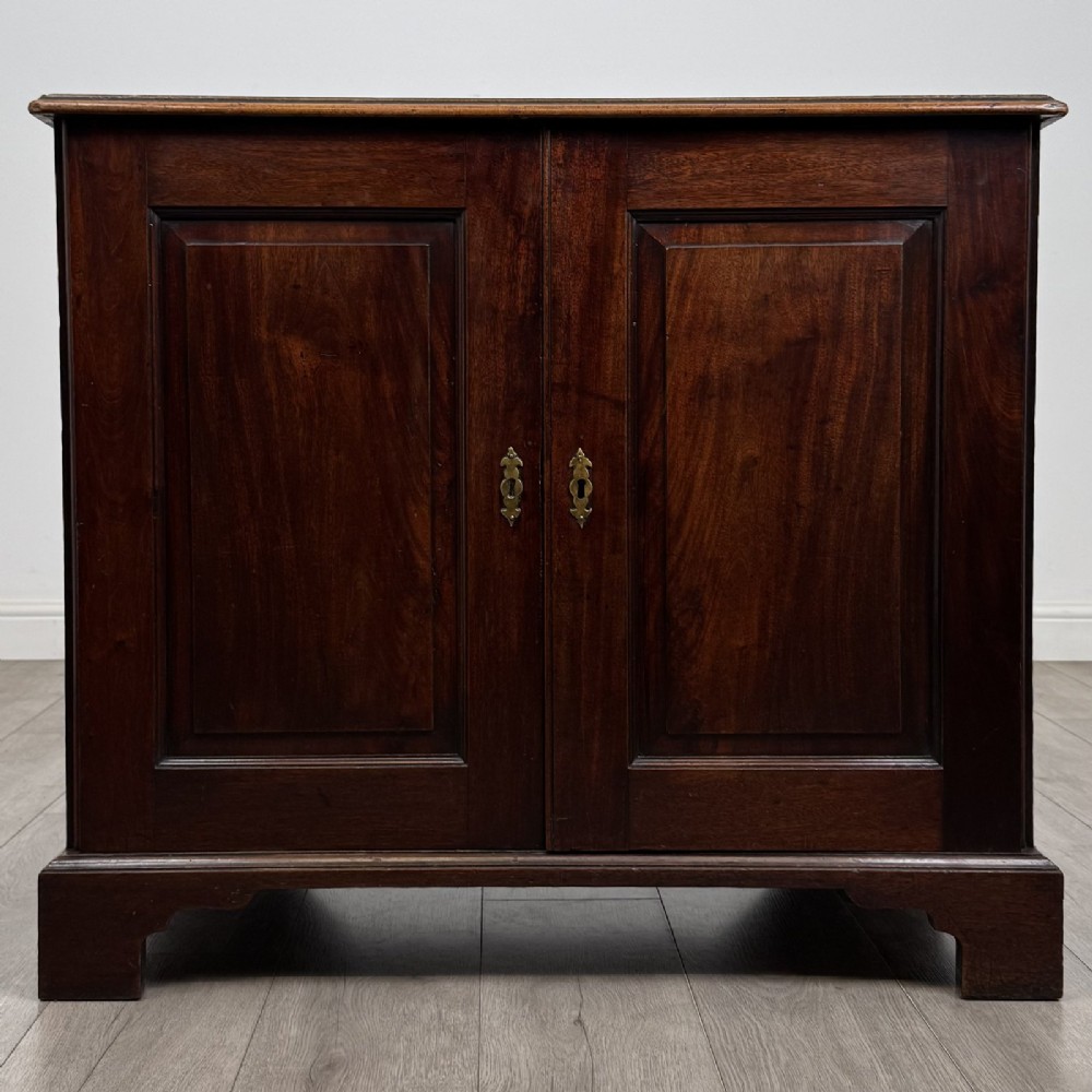 An 18th-century dark mahogany low cupboard featuring twin panelled doors with brass keyhole escutcheons resting on bracket feet.