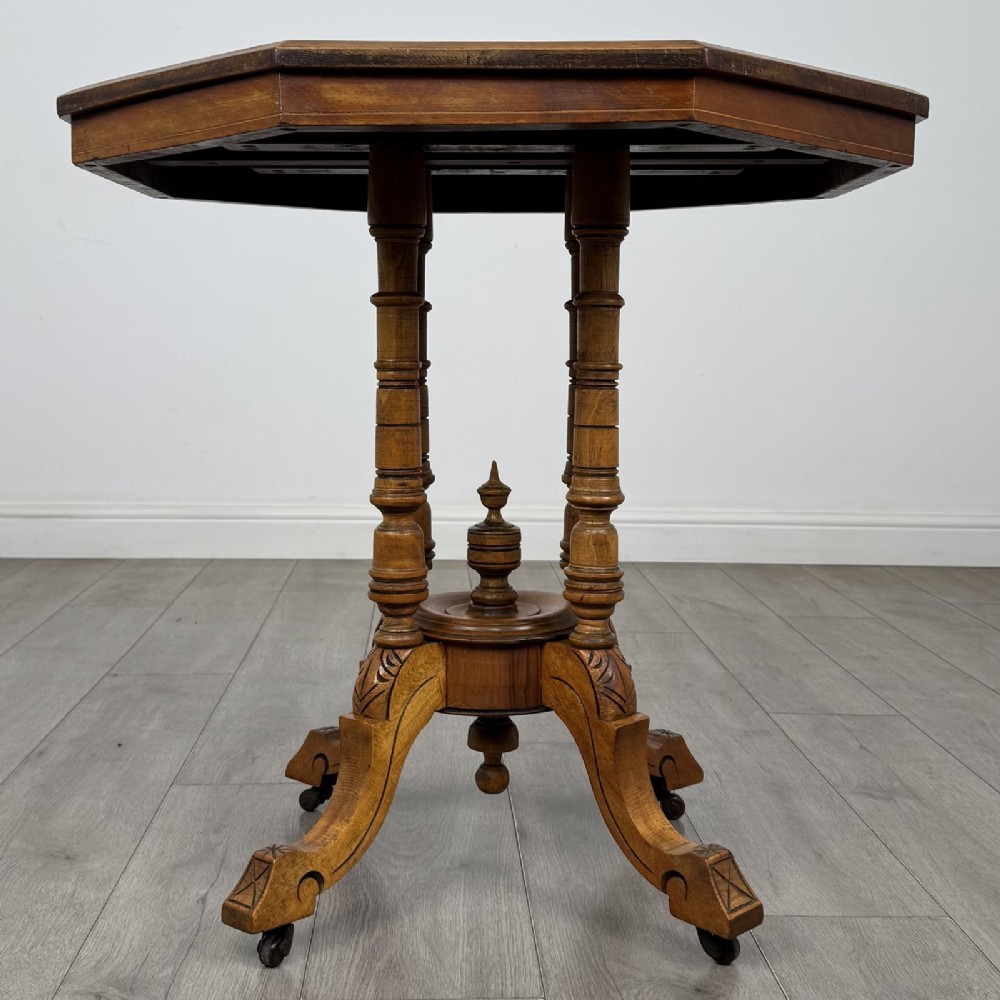A Victorian octagonal walnut side table featuring turned support columns, a central finial, and carved splayed legs with castors.