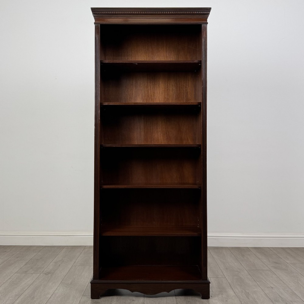 A tall dark mahogany open bookcase featuring a dentil cornice, five fixed shelves, fluted side pilasters, and a shaped apron base.
