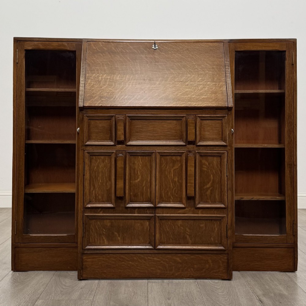An Art Deco oak side-by-side bureau bookcase with a central slant-front desk above panelled cupboards, flanked by two glazed display cabinets.
