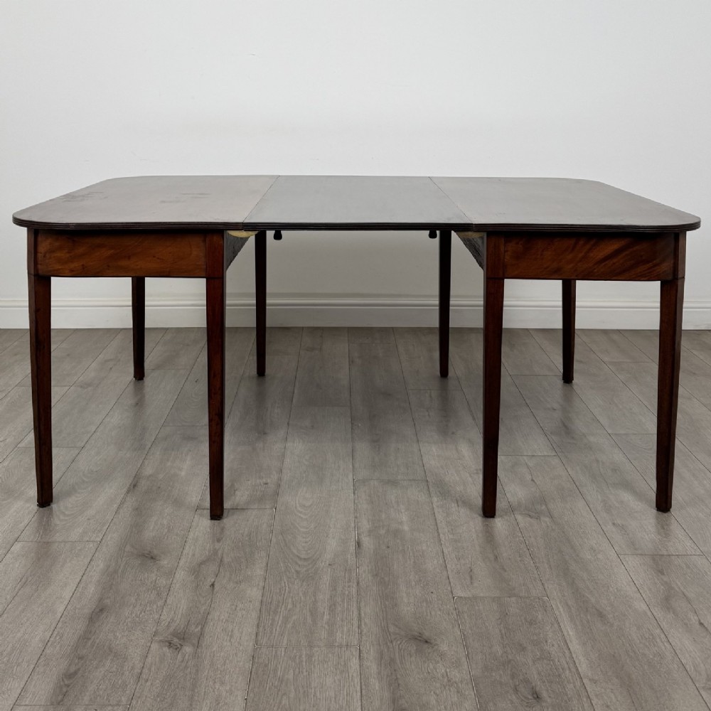 An antique Georgian dark mahogany extending dining table featuring rounded D-end corners, a removable leaf, and square tapered legs.