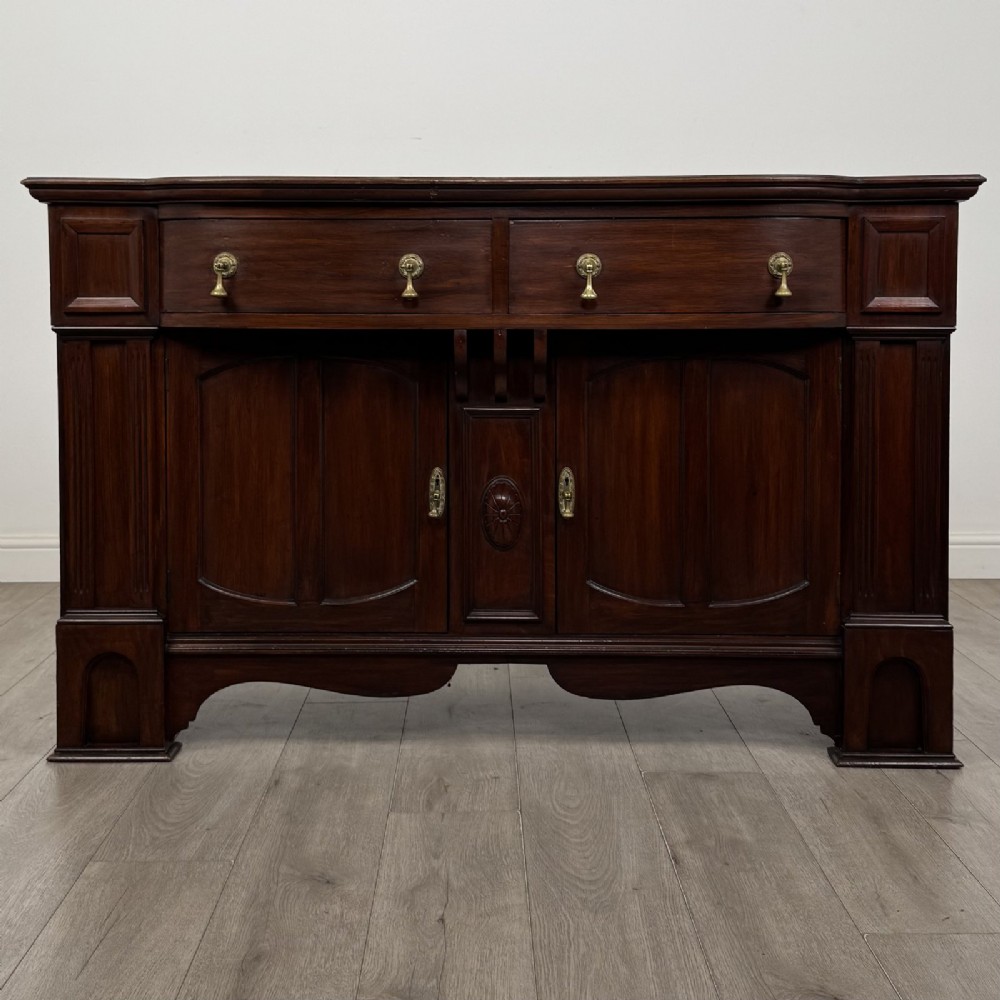 An Edwardian dark mahogany bow-front sideboard featuring two drawers with brass drop handles over a double cupboard with carved details.