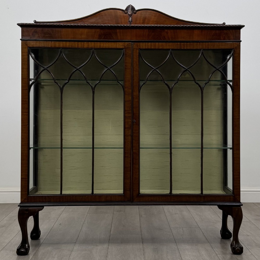 A dark mahogany glazed display cabinet featuring gothic astragal door bars, a carved pediment top, and cabriole legs with ball and claw feet.