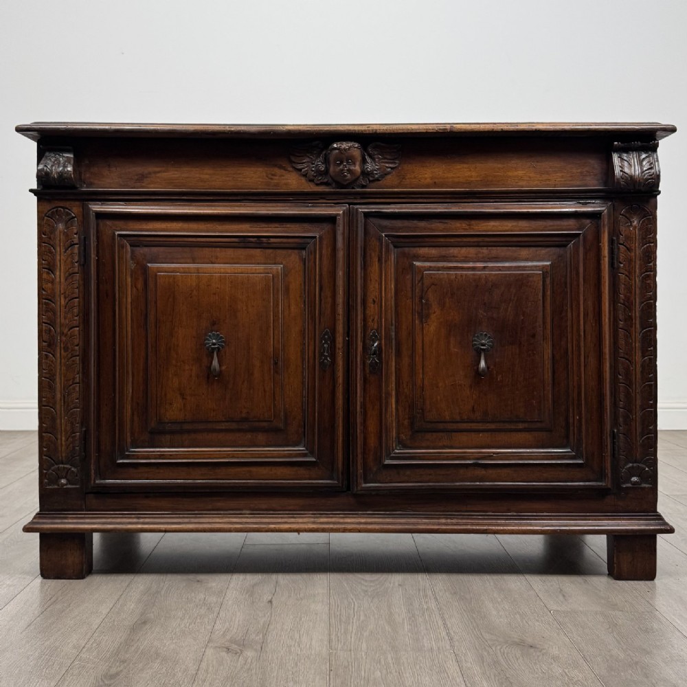 A 19th-century French dark walnut sideboard featuring twin panelled doors with drop handles, flanked by fluted pilasters, with a carved winged cherub head centred on the frieze.