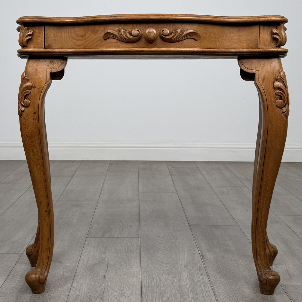 A light oak French-style console table featuring a serpentine front, carved relief details on the apron, and cabriole legs.