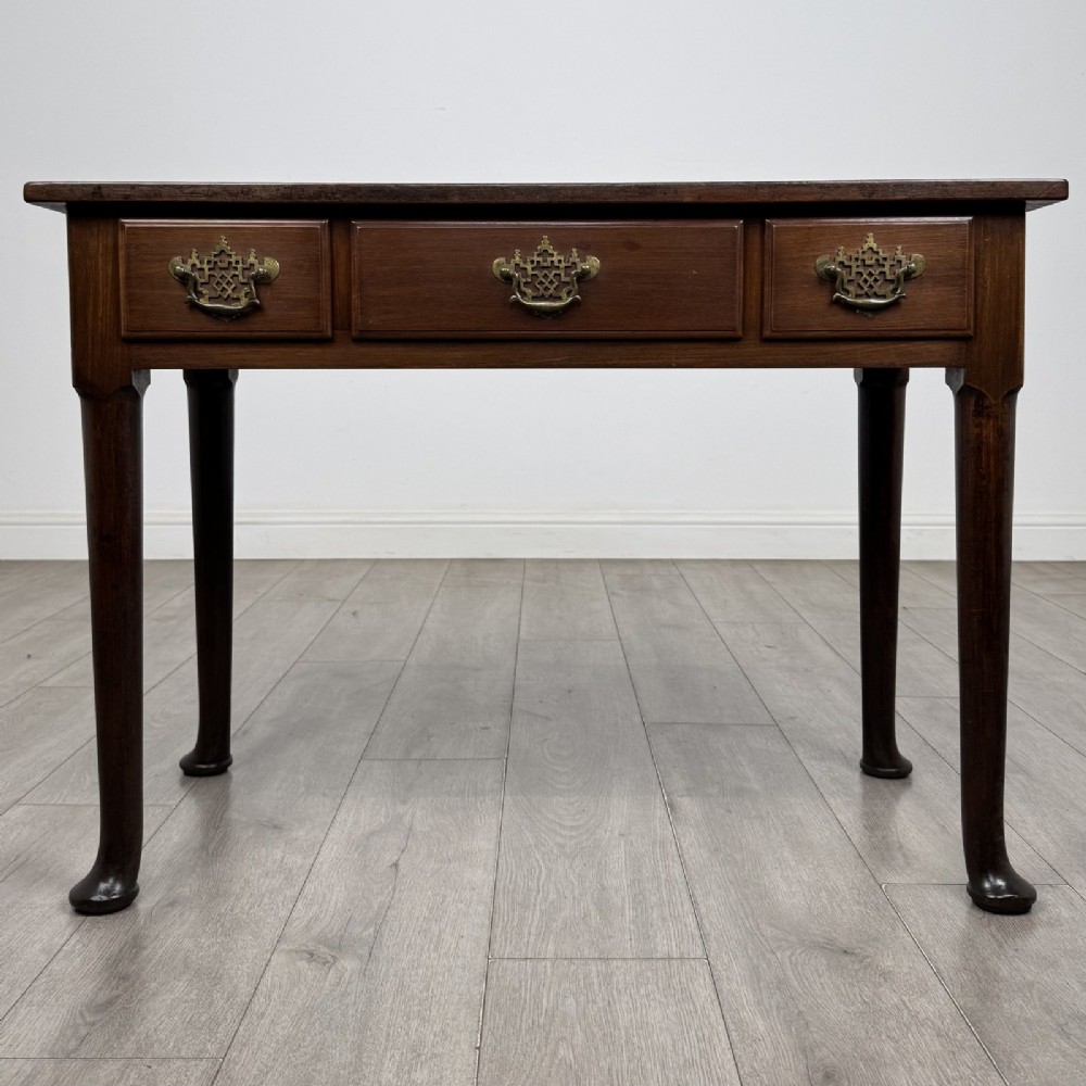 A dark mahogany Georgian style side table featuring three drawers with ornamental brass handles and four tapered legs with pad feet.