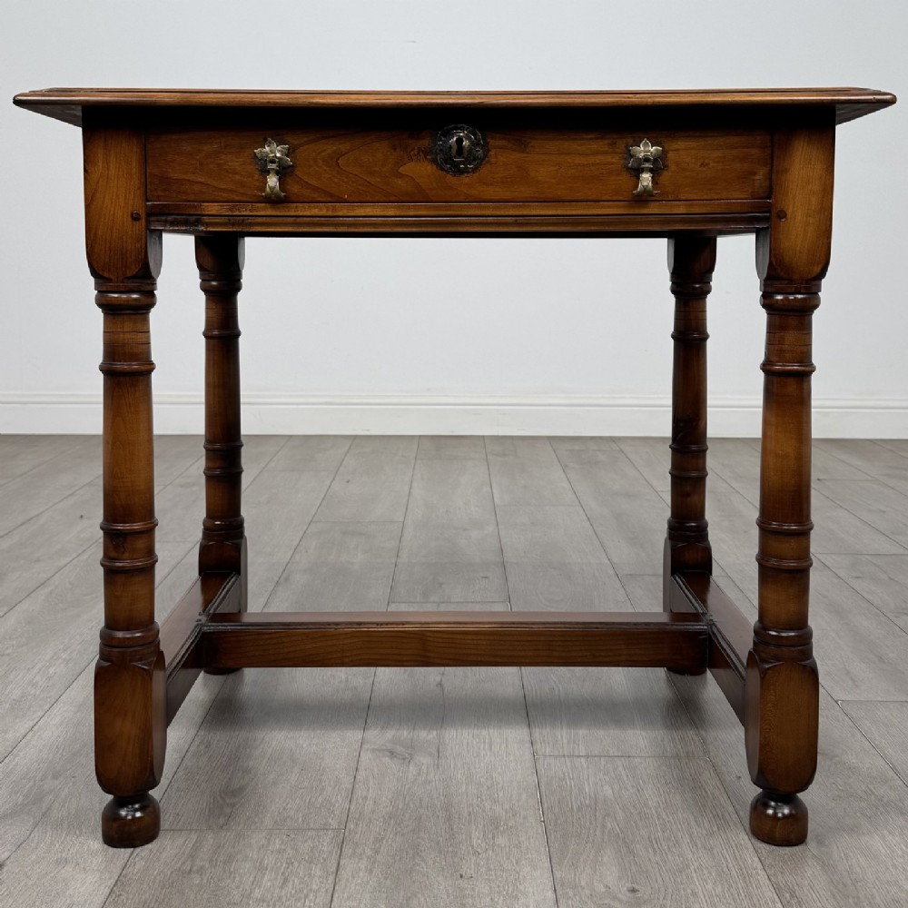 A warm brown fruitwood side table featuring a single drawer with twin brass drop handles, turned legs, and an H-stretcher.