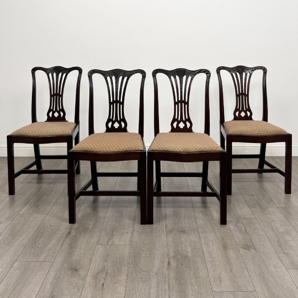 A set of four dark mahogany dining chairs featuring carved pierced splats, straight square legs with H-stretchers, and patterned upholstered seats.