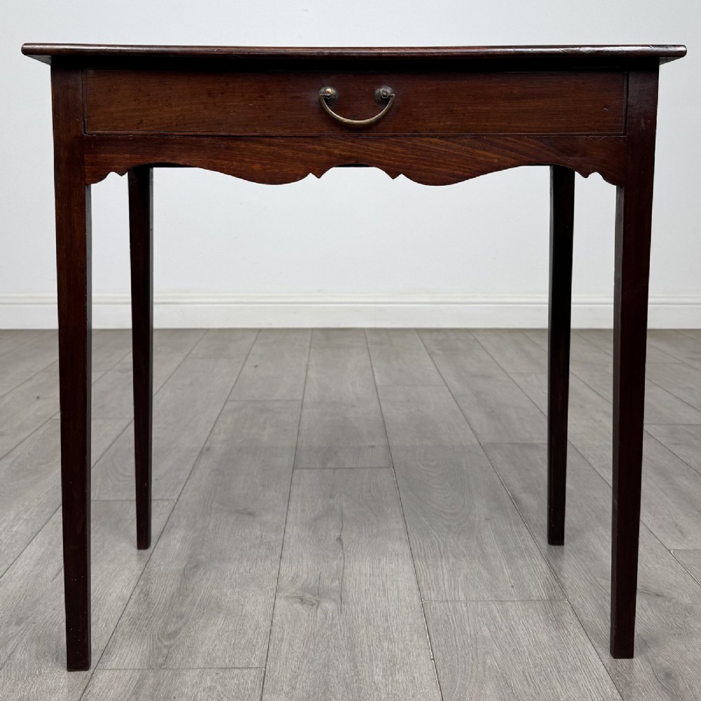An 18th-century Georgian mahogany side table with a single frieze drawer, brass handle, shaped apron, and straight square legs.
