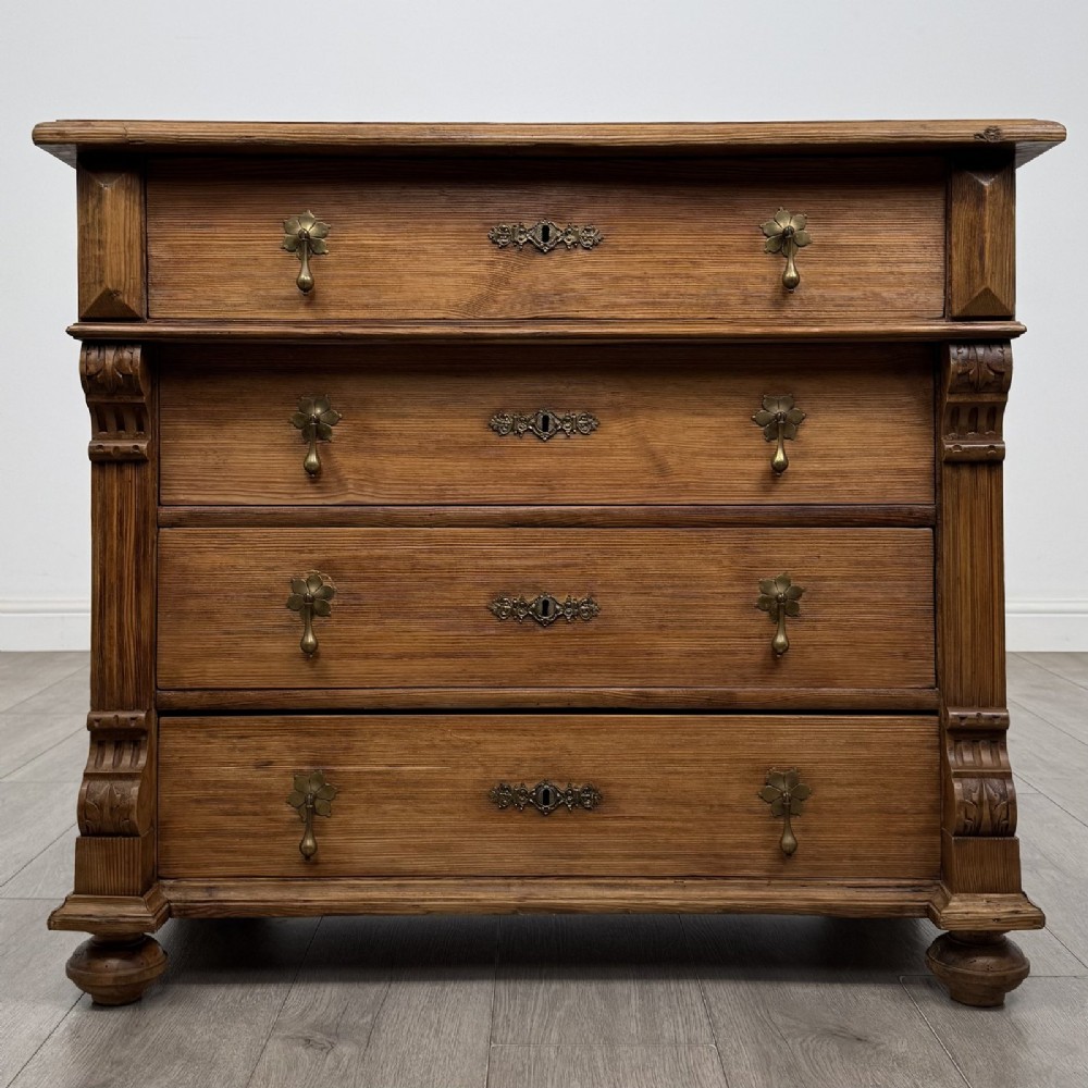 An antique Victorian pine chest of four drawers featuring ornamental metal drop handles and carved architectural pilasters on turned feet.
