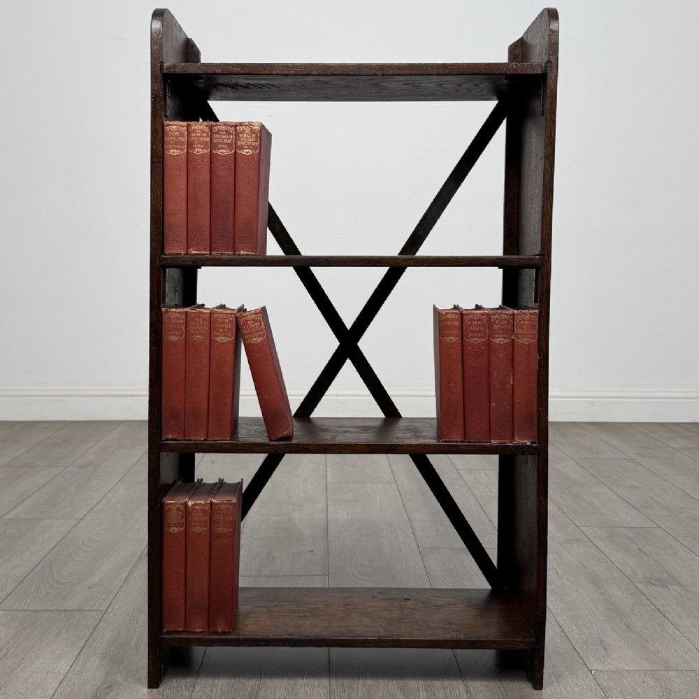 An open dark oak bookcase featuring three shelves and a black iron cross back stretcher.
