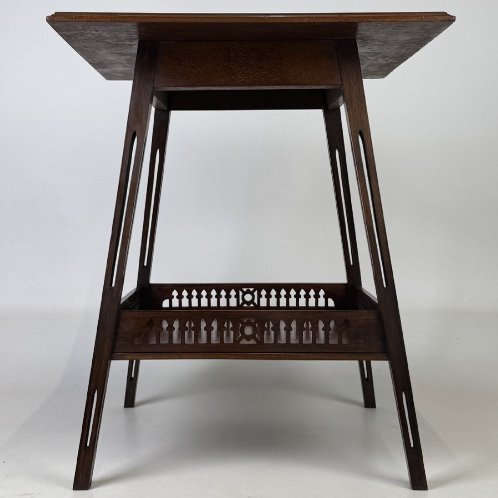 An Edwardian dark mahogany lamp table featuring splayed legs with elongated vertical cutouts and a lower shelf enclosed by a carved fretwork gallery.