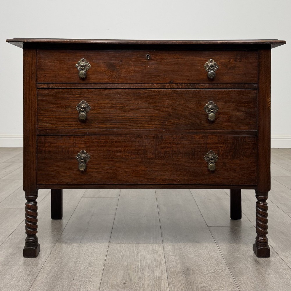 A dark oak chest of drawers featuring three full-width drawers with metal drop handles and front barley twist legs.