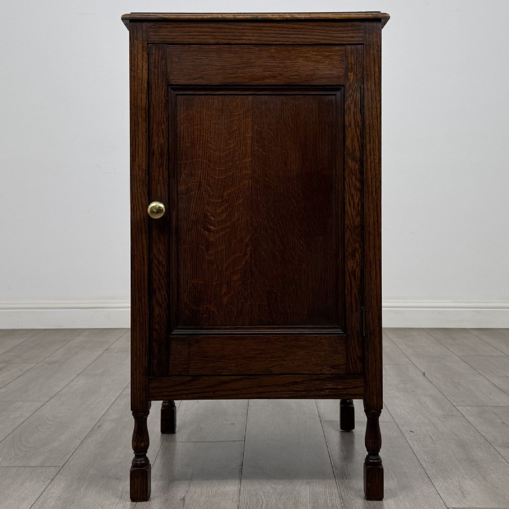 A dark brown oak record cabinet featuring a single panelled door with a brass knob and turned legs.