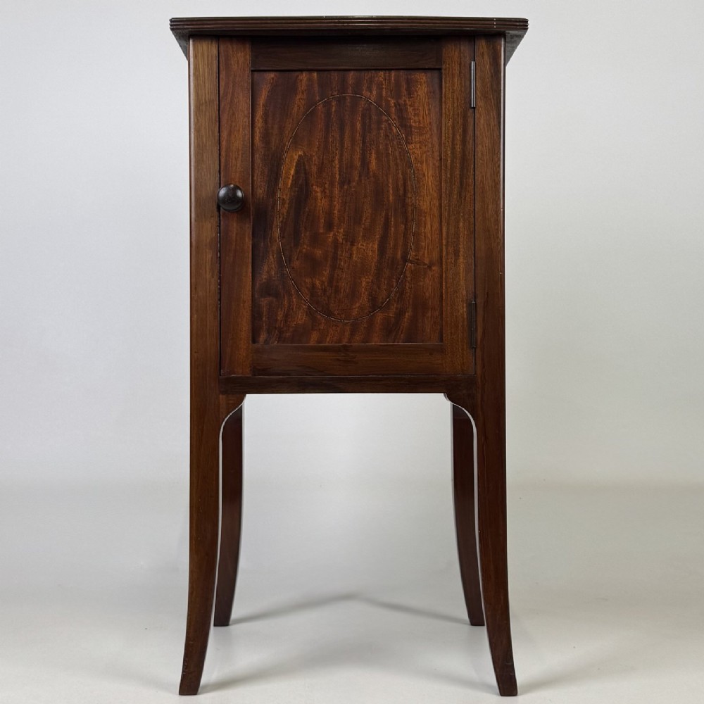 An Edwardian mahogany bedside cabinet with an inlaid oval door panel and slim square tapered legs.