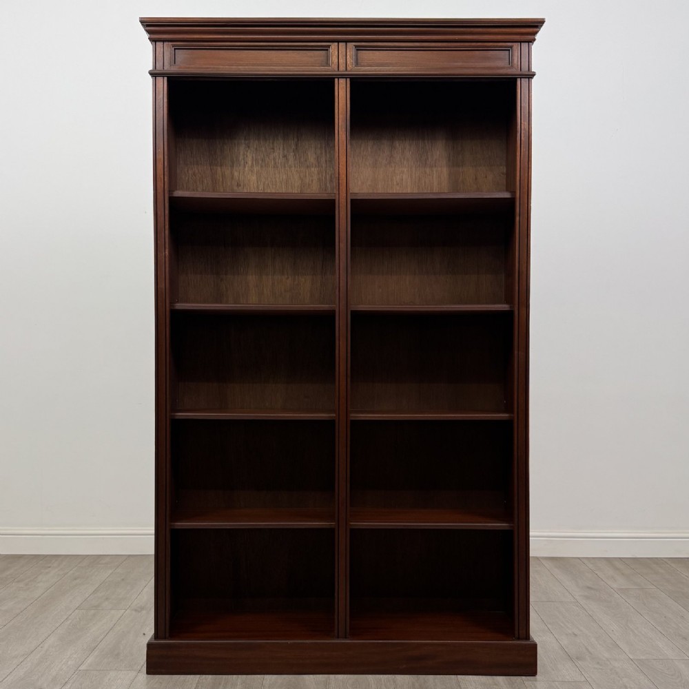 A tall, dark mahogany double-bay open bookcase featuring multiple shelves, a moulded cornice top, and a solid plinth base.