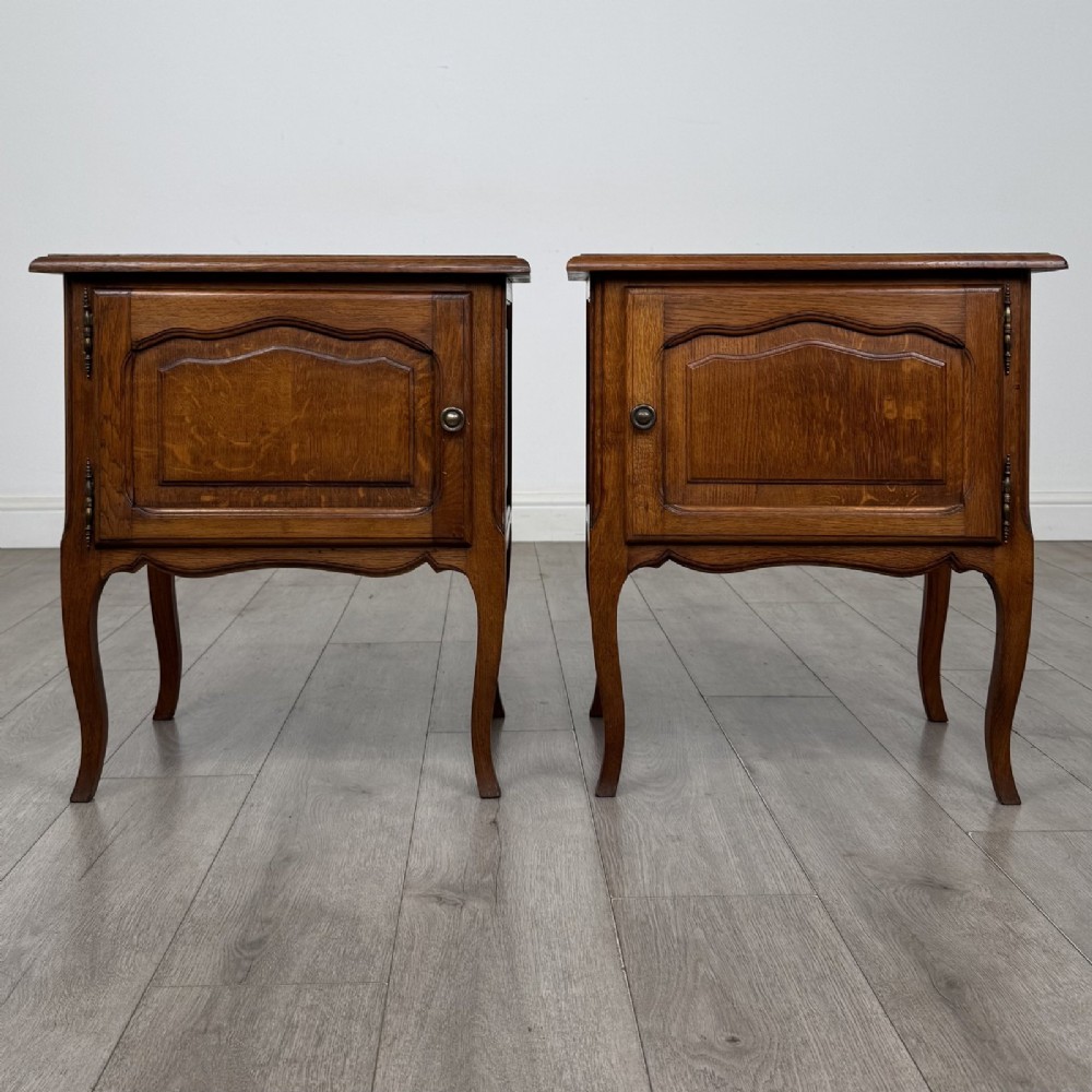 A matching pair of vintage warm oak French style bedside cabinets featuring cabriole legs, single panelled doors, and metal knobs.