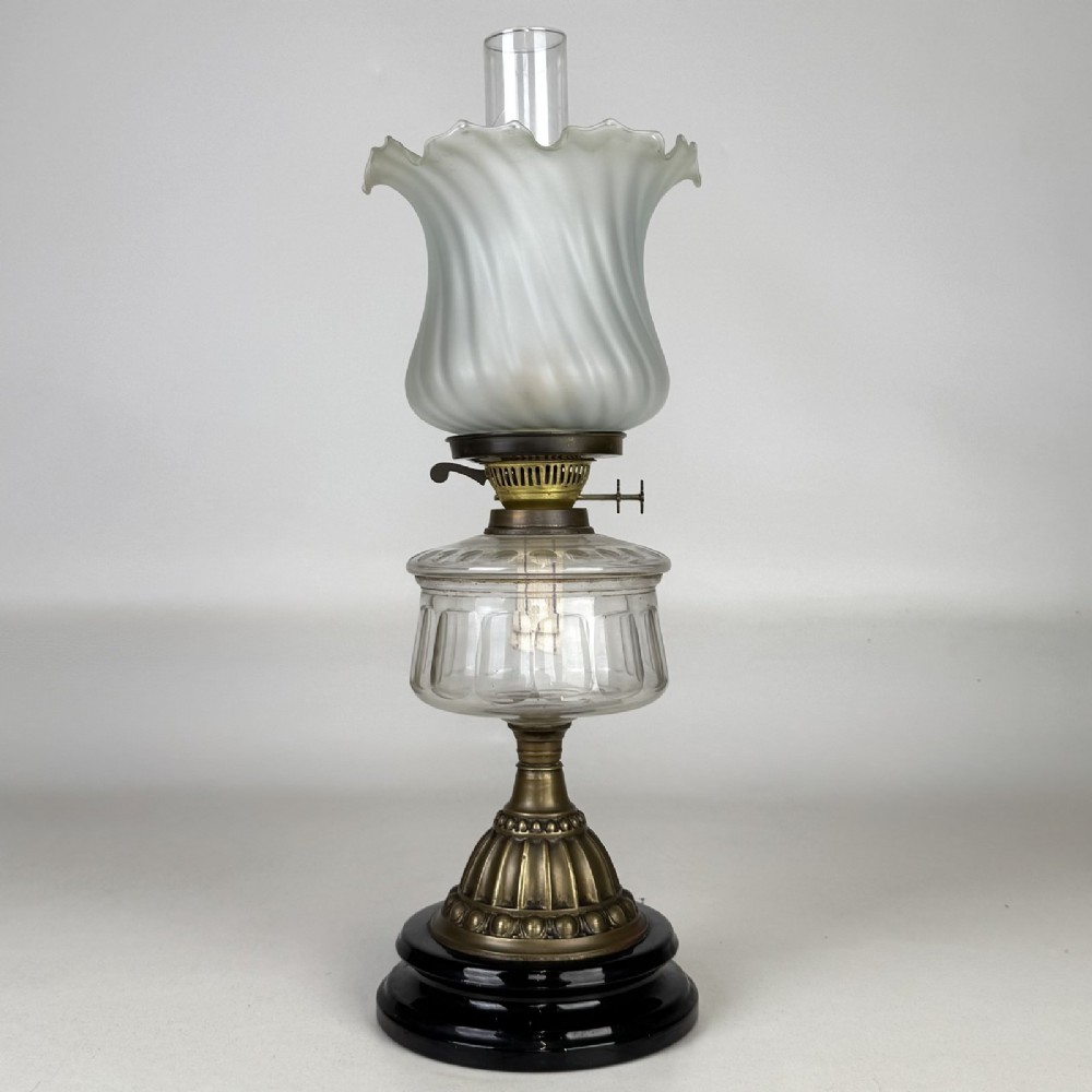 A Victorian brass oil lamp with a black stepped base, a cut glass reservoir, an exposed glass chimney, and a swirled frosted glass shade with a ruffled rim.