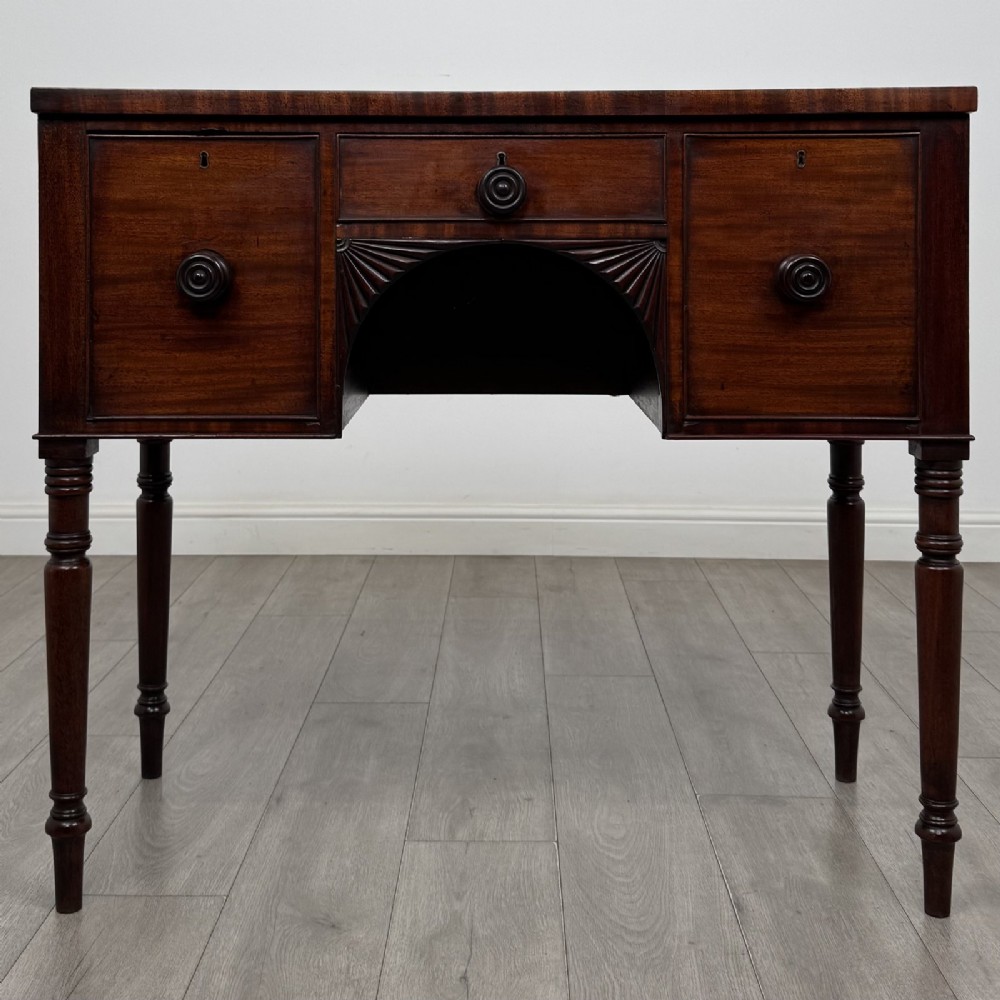 A Regency mahogany kneehole sideboard featuring turned legs, flame mahogany drawer fronts, and fan-carved spandrel corner details.