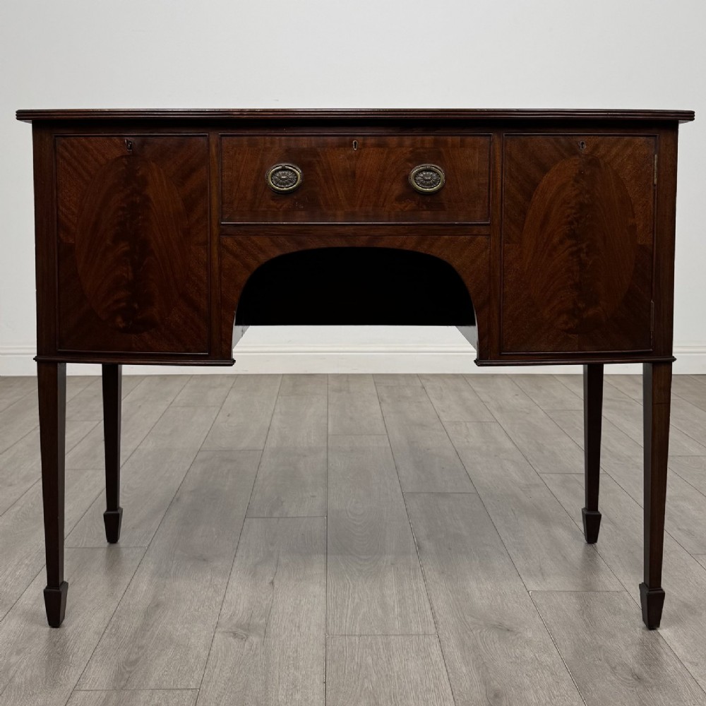 A mahogany bowfront sideboard featuring two oval-inlaid cupboard doors flanking a central drawer, set upon four square tapered legs with spade feet.