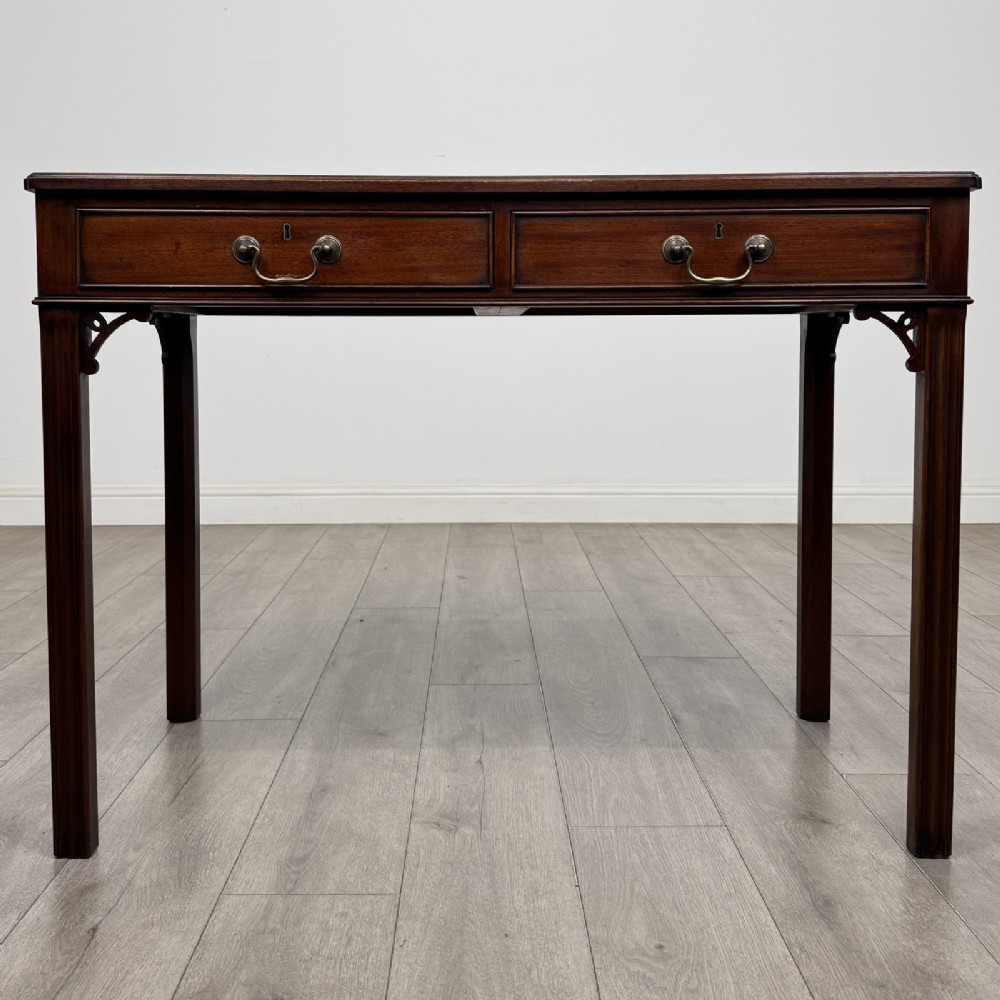 A dark mahogany Chippendale style writing desk featuring two drawers with brass handles, straight fluted legs, and corner fretwork brackets.