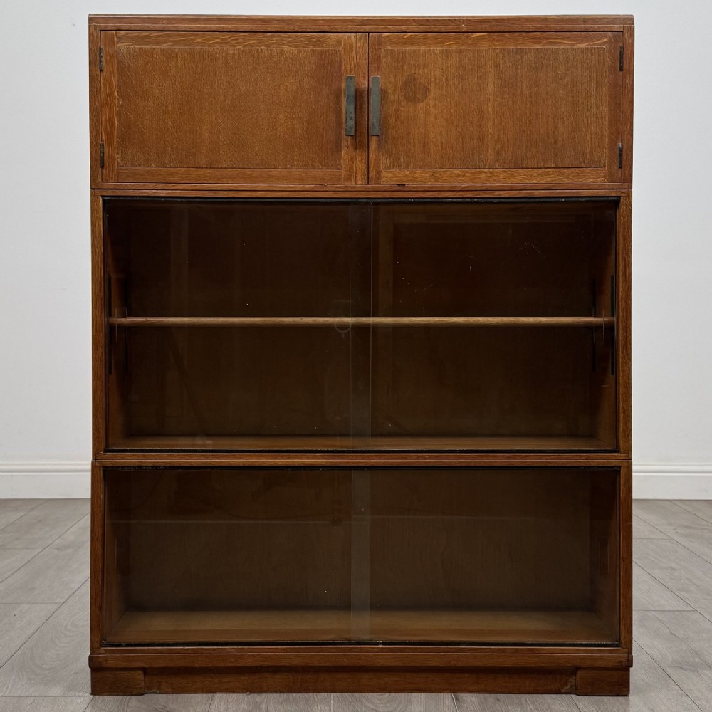 A 20th-century oak stacking bookcase featuring a double-door wooden top cabinet above two tiered sliding glass door compartments.