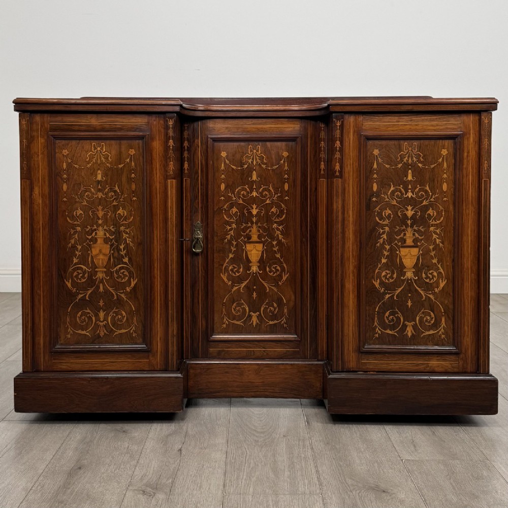 A dark rosewood Victorian breakfront sideboard with three cupboard doors featuring intricate satinwood urn and scroll marquetry inlays.