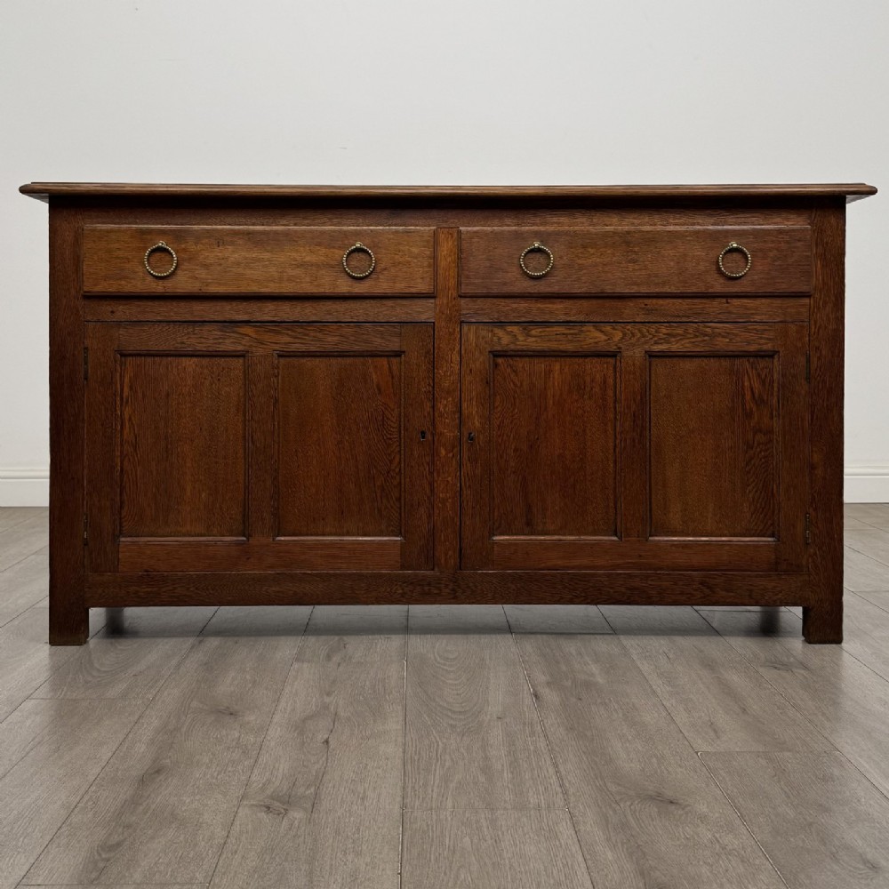 A dark oak early 20th-century sideboard featuring two top drawers with circular brass ring pulls over two panelled cupboard doors.